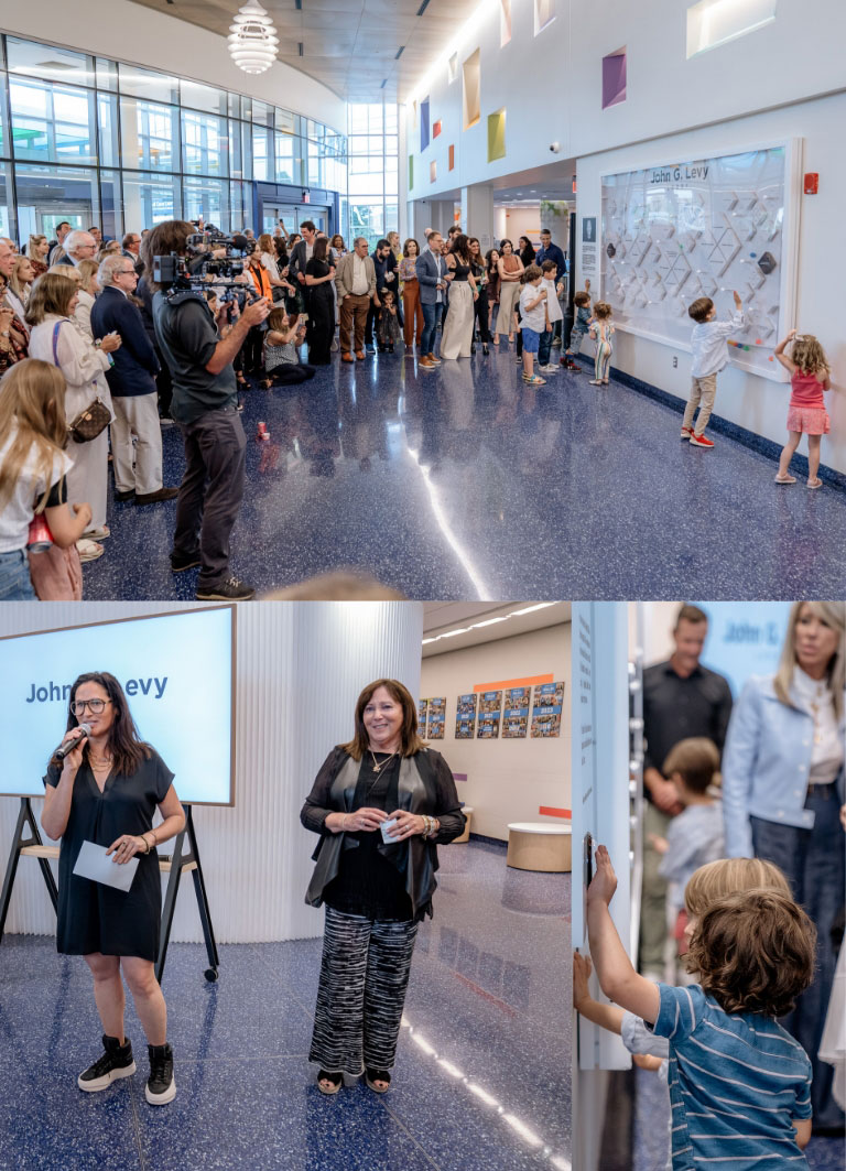 A crowd gathers in a bright, modern lobby for an unveiling event. Children interact with a wall display, while adults observe. Two women speak on a stage, and a young boy closely examines the display.